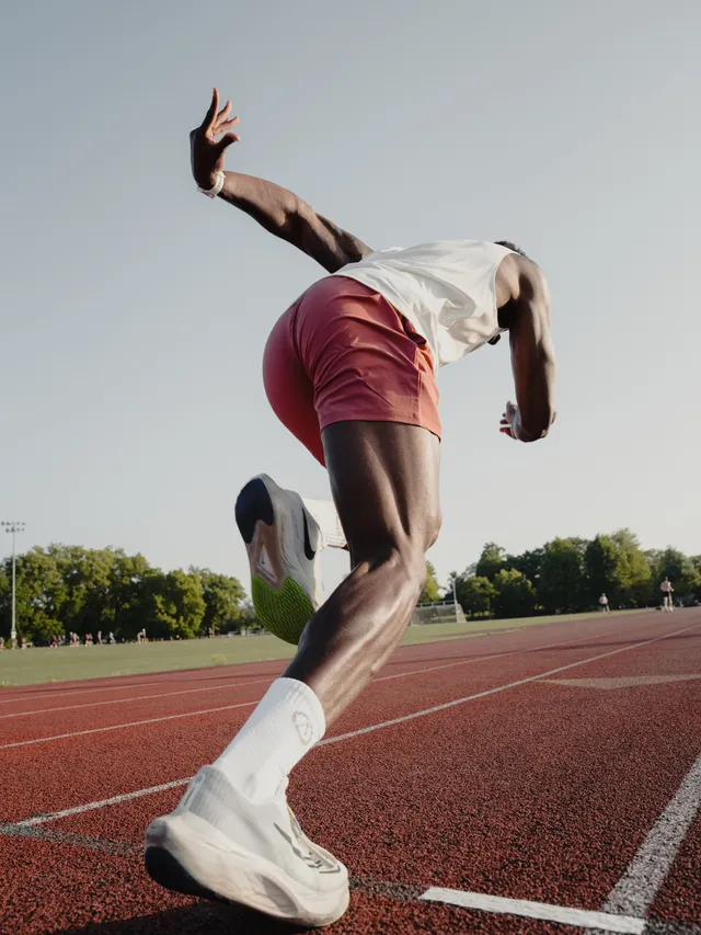 A dynamic and athletic moment captured through editorial photography, featuring a male runner in motion on an outdoor track. The image dominates with warm tones of red and earthy brown, conveying a sense of energy and determination.