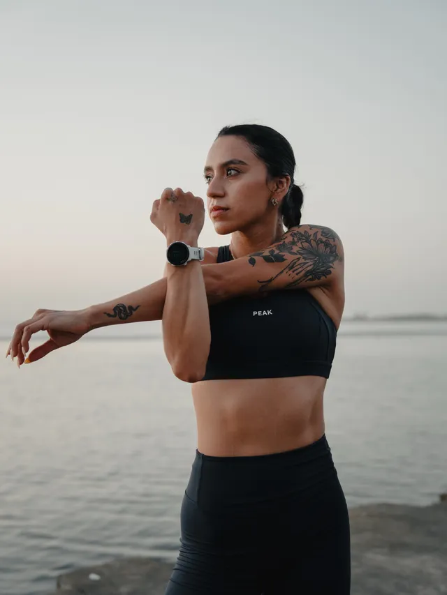 A woman posing confidently at the edge of a body of water during twilight, showcasing athletic wear. The scene exudes a calm yet empowered mood with a natural color palette of soft blues and warm neutrals.