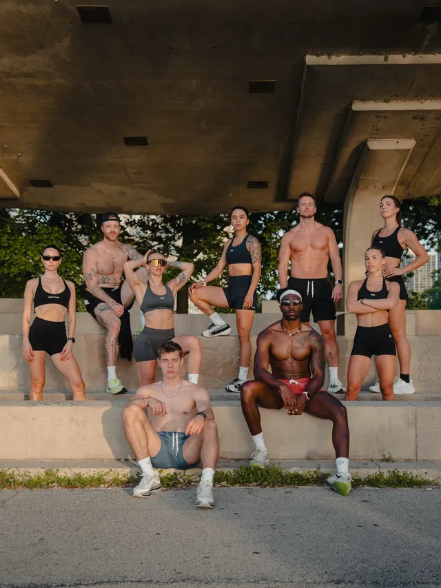 A group of athletic individuals posing confidently under an architectural structure, showcasing their fitness. The medium is editorial photography with a vibrant, summery mood, dominated by earthy tones and natural skin colors.