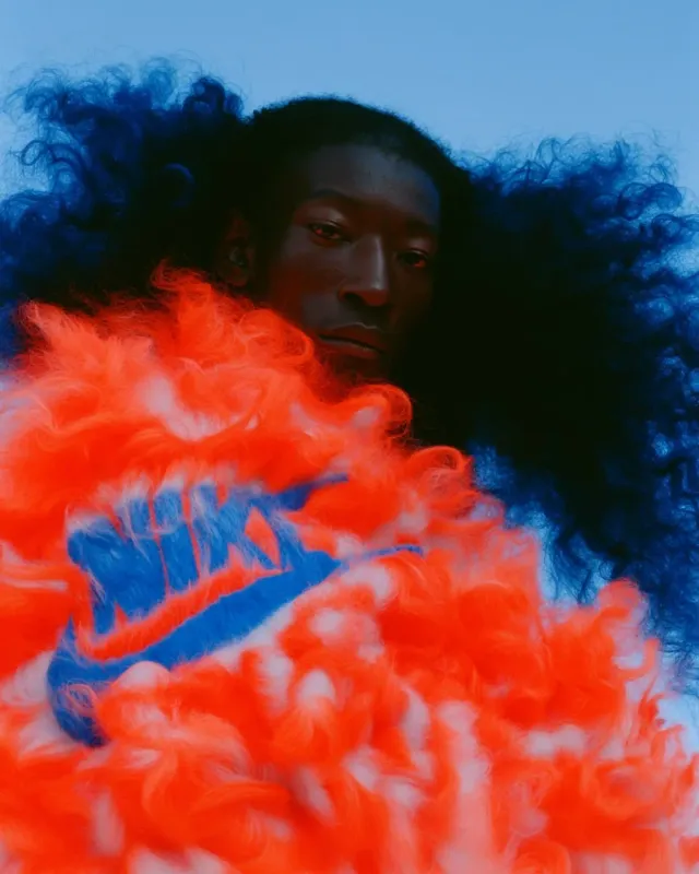 A portrait of a person featuring vibrant orange and blue fur-like textures. The image has a surreal and playful mood, with a focus on bold colors and striking patterns.