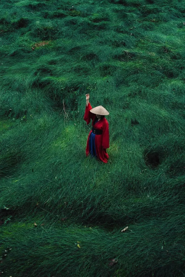 Woman in red and blue clothing standing on green grass in a tranquil setting.