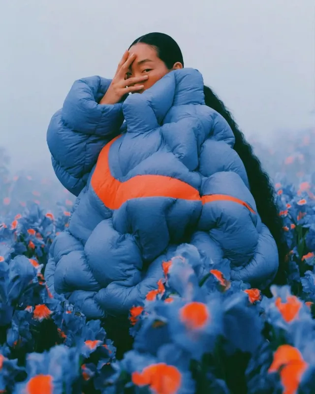 A woman in blue outerwear stands in a field of blue flowers.