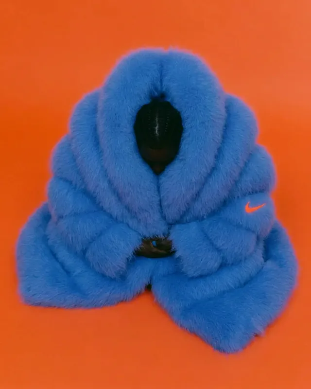 Full-figure portrait of a person in a blue faux fur garment with an orange background.