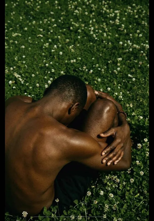 A man seated in a grassy field, with rich green grass and earthy skin tones.