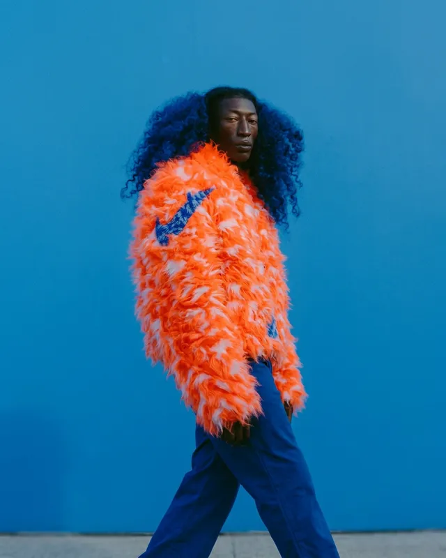 Portrait of a man in an orange feathery coat with a blue background.