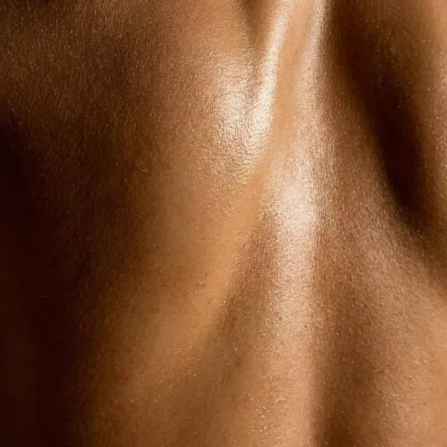 A close-up of glistening skin, showcasing the smooth, textured surface and highlights. This editorial photograph exudes a luxurious atmosphere with warm, earthy tones dominating the palette.