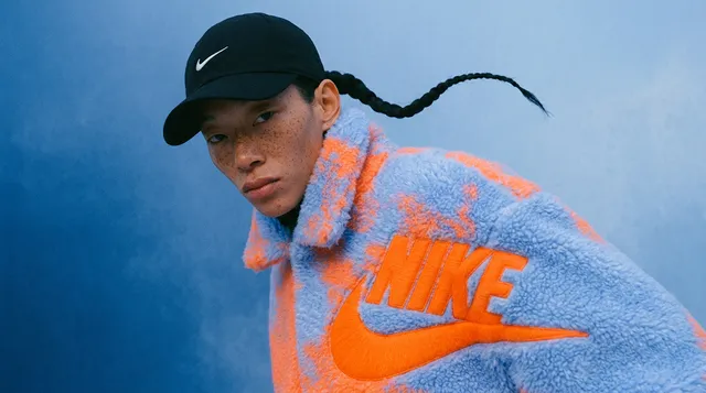 Young man wearing a vibrant fleece jacket with a logo on a blue background.
