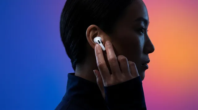 A profile view of a woman placing her finger on an earbud, illuminated by vibrant gradient lighting that shifts from blue to orange. This editorial photograph captures a modern and tech-savvy vibe with a focus on contemporary design.