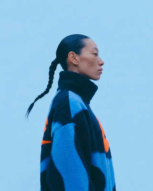 Profile portrait of a woman in a colourful oversized sweater on a blue background.