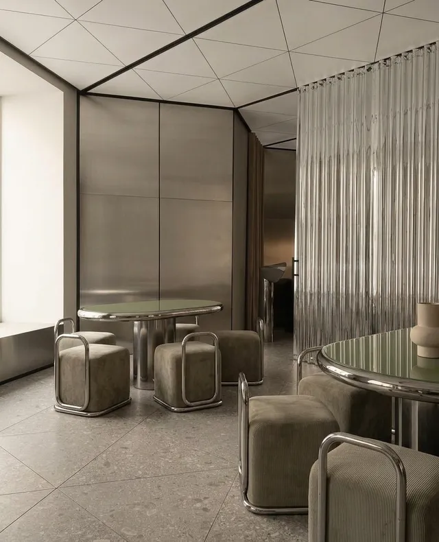 A serene interior scene featuring modern furniture with sleek metal accents and soft, muted tones. The composition emphasizes a minimalist design style, highlighting textures and surfaces in a contemporary setting.