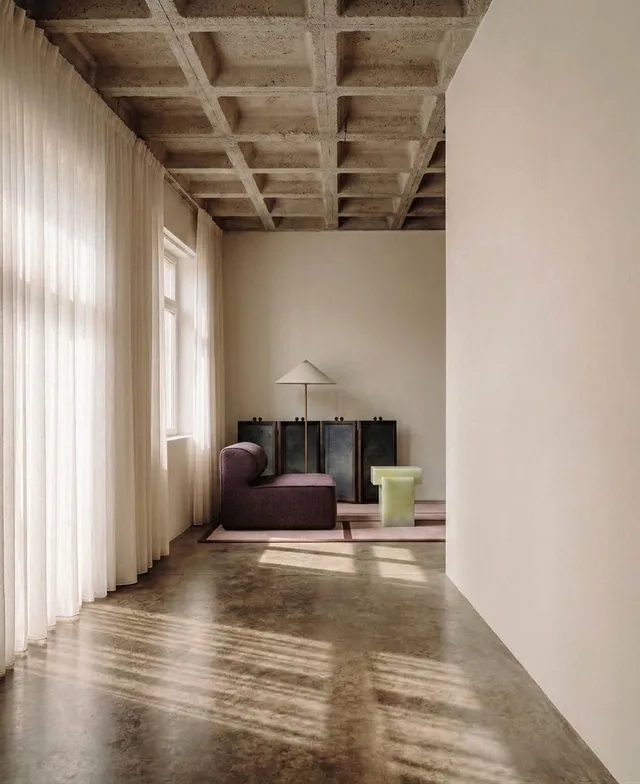 An interior scene showcasing minimalist design, featuring a sofa and unique furniture against soft, warm tones. The photograph captures natural light streaming through sheer curtains, creating a serene and inviting atmosphere.