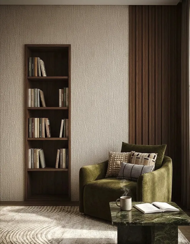 An inviting interior scene featuring a cozy green armchair with patterned cushions next to a stylish bookshelf filled with books, complemented by a soft textured wall and a sleek marble table. The mood is serene with warm, earthy tones dominating the color palette.